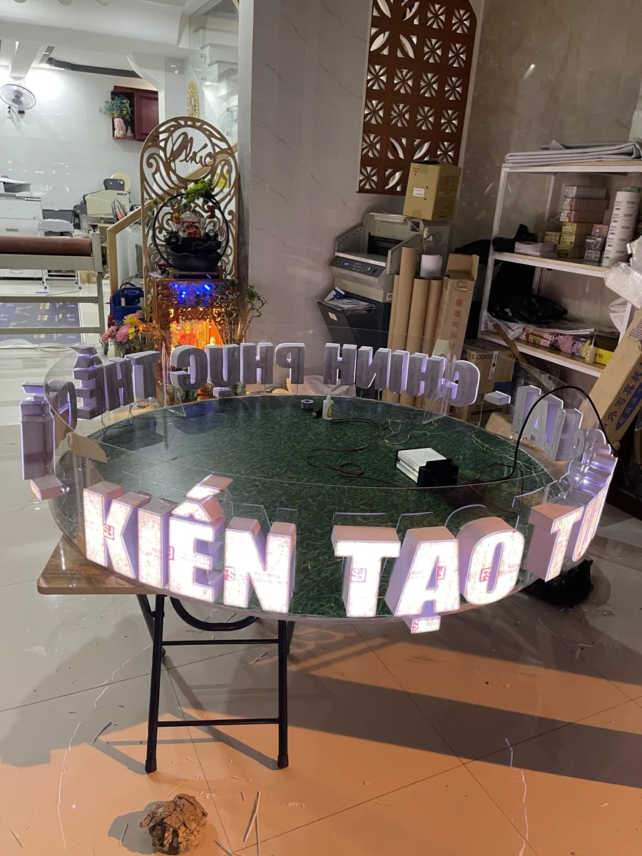 Dãy chữ nổi gắn LED đang phát sáng đặt trên bàn tròn tại xưởng In Đức Lộc