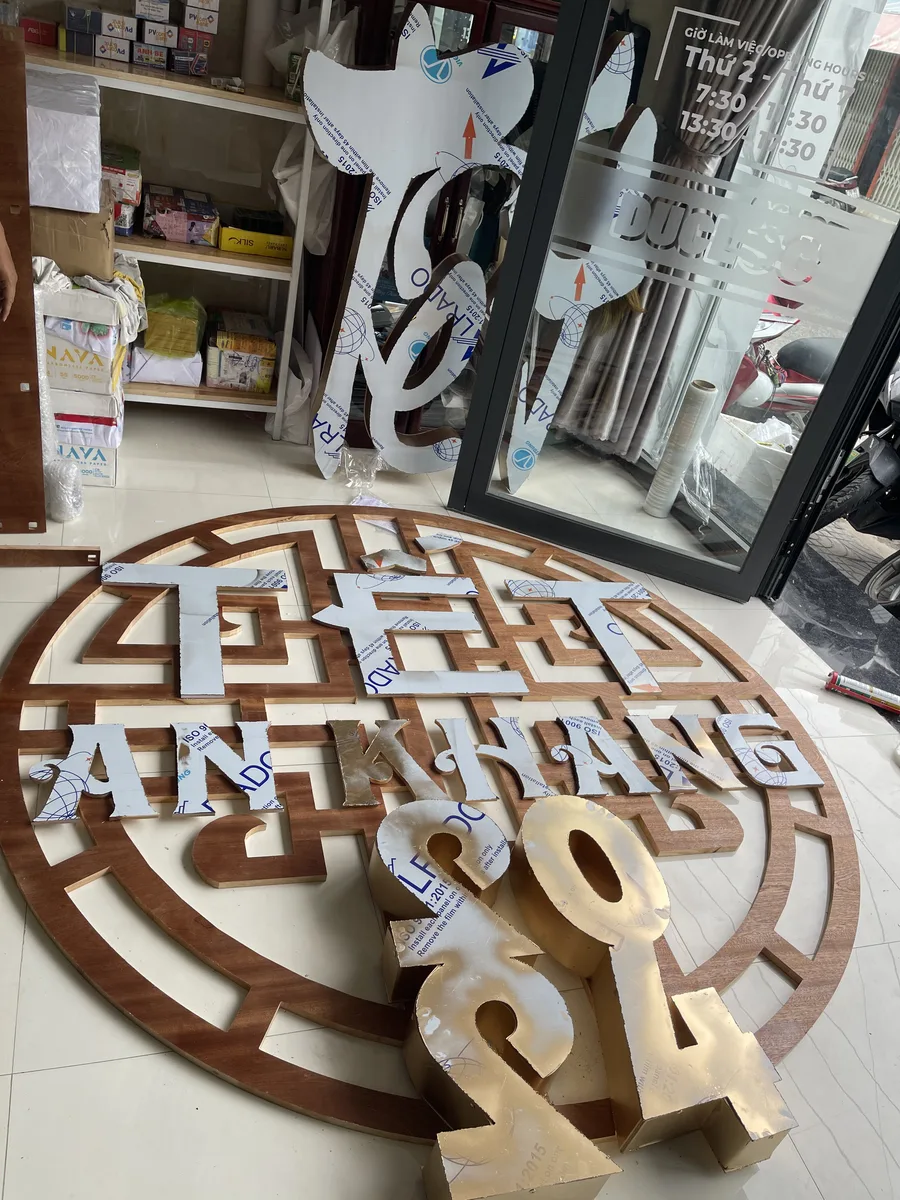Bộ chữ Thịnh An Khang còn màng bảo vệ đặt trên khung tròn cắt CNC tại xưởng In Đức Lộc, phía trước là chữ số vàng gương