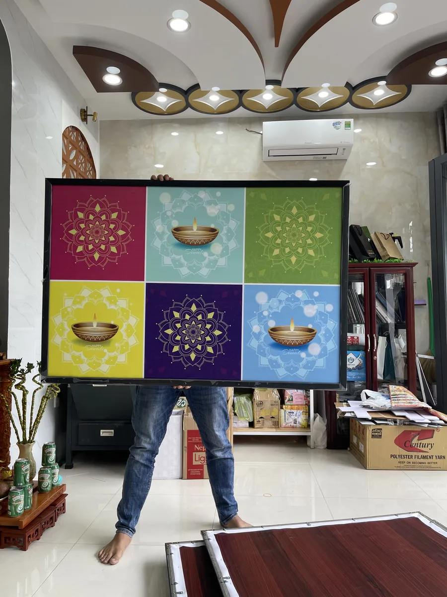Bức tranh canvas khổ lớn họa tiết mandala và đèn dầu sáu ô màu, nhân viên In Đức Lộc cầm kiểm tra tại xưởng
